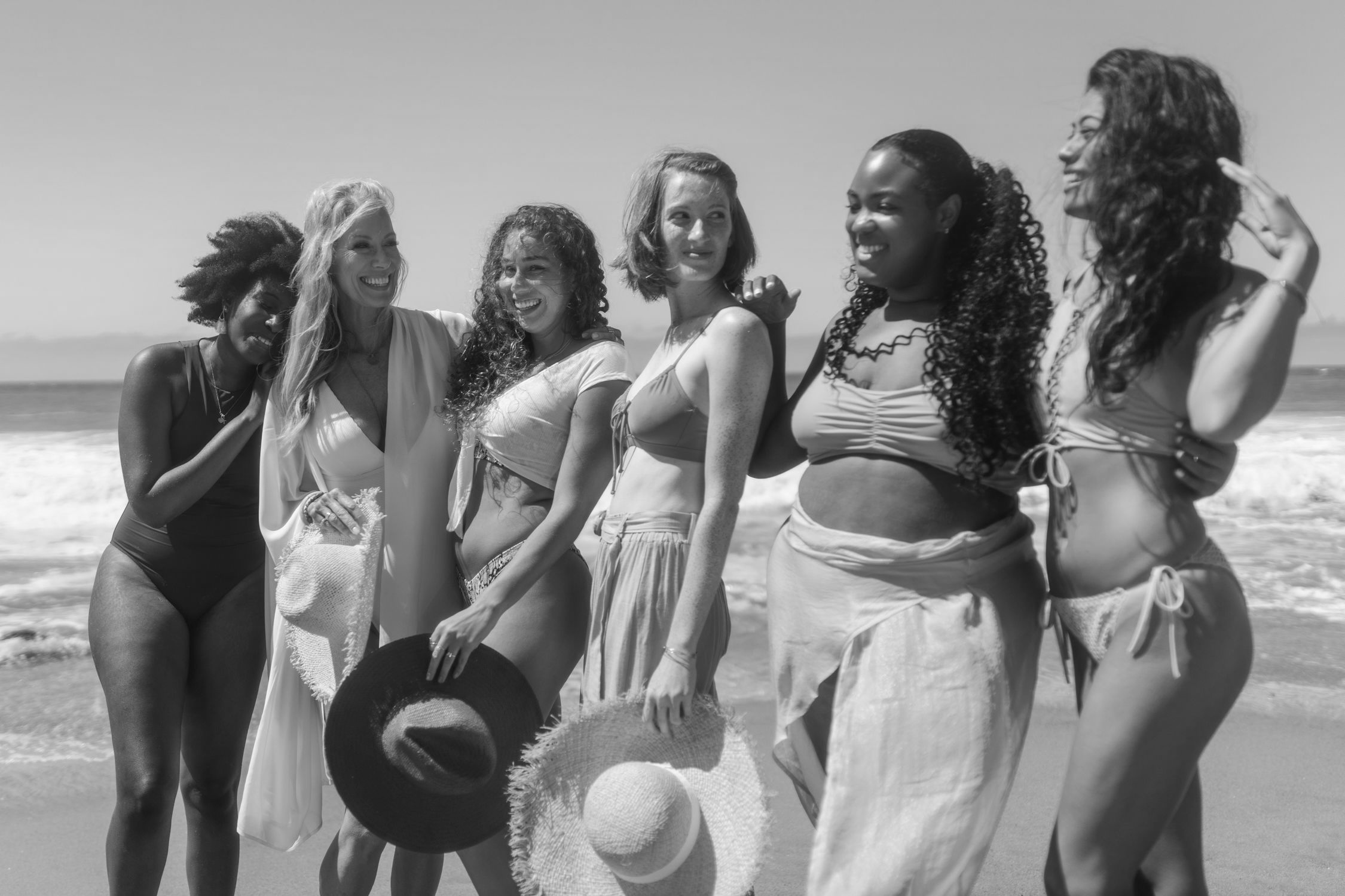 A diverse group of women standing together on a beach, arms raised in celebration